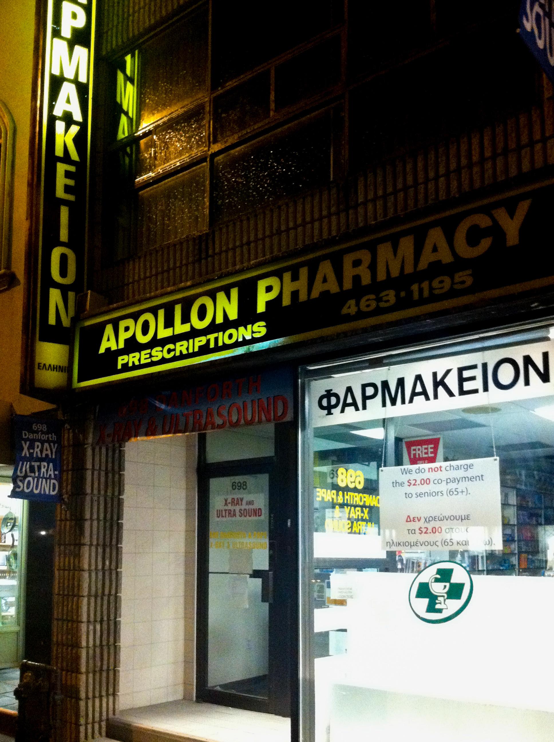 The exterior of Apollon Pharmacy at night, with a bright yellow sign and Greek text reading "ΦΑΡΜΑΚΕΙΟΝ" on the window.